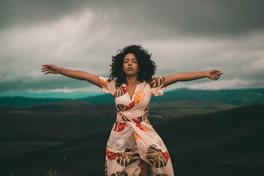 A woman in a flowing dress enjoys peaceful moments in a vast, cloudy landscape.