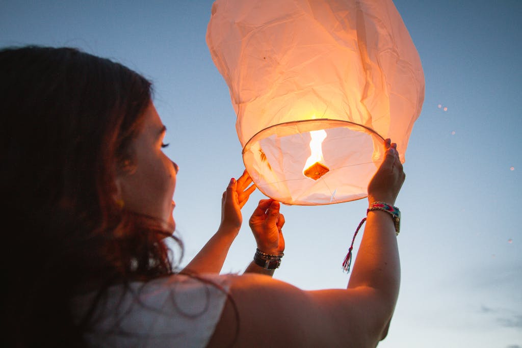 A woman releases a glowing paper lantern at dusk, symbolizing hope and celebration.