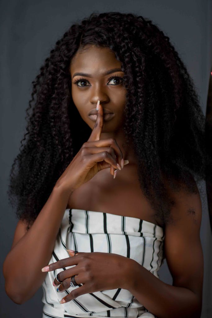 Portrait of a woman with finger on lips, indicating silence, on a dark background.