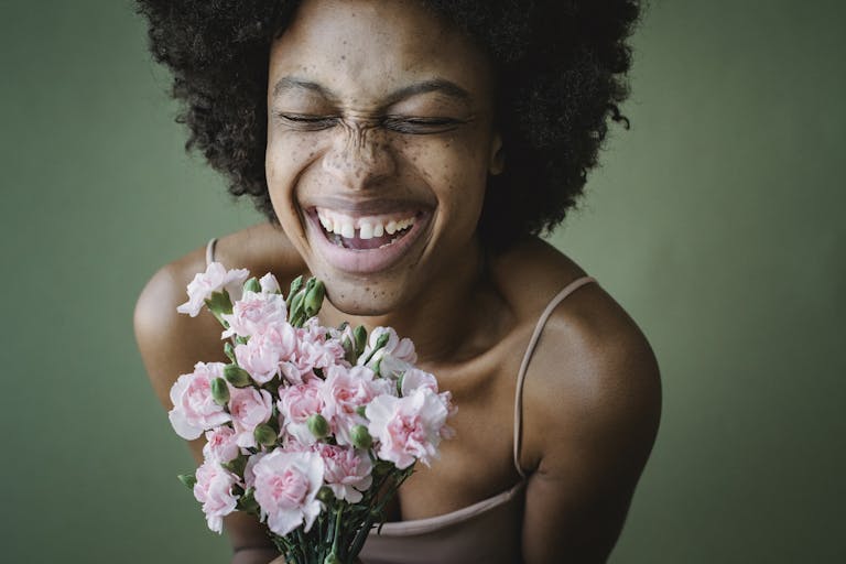 A cheerful woman with a radiant smile holding a pink carnation bouquet against a green background.