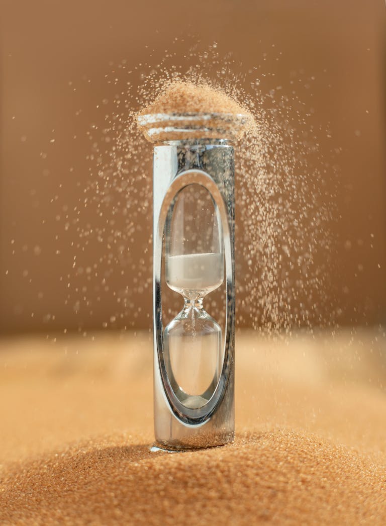 Close-up of an hourglass with sand falling, capturing the essence of time against a yellow background.