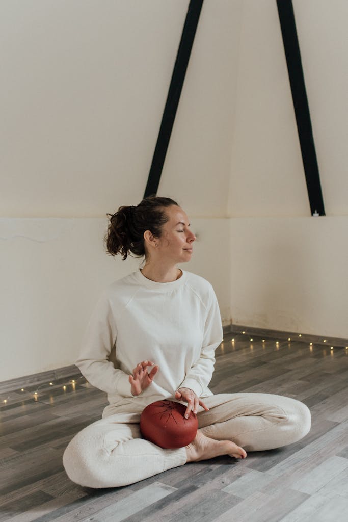 Relaxing indoors meditation session with woman playing tank drum, eyes closed in peaceful ambiance.