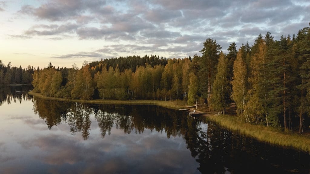 Peaceful fall landscape of a Finnish lake surrounded by vibrant autumn trees and reflections, perfect for nature lovers.